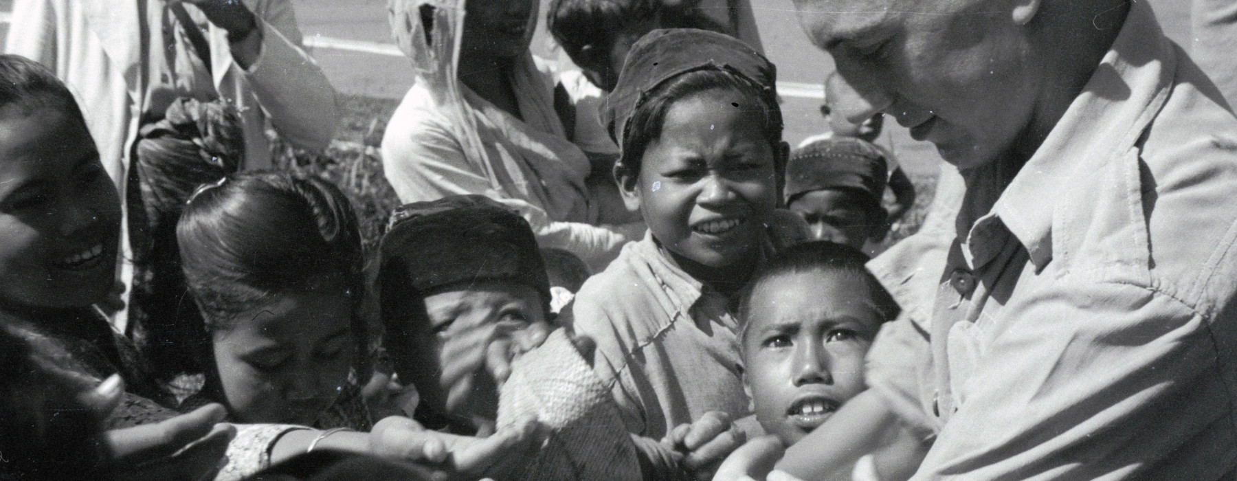 Uitdelende Nederlandse militair omringd door kinderhanden tijdens de feestelijkheden in Cipanas (Java) © Erven C.J. Taillie 