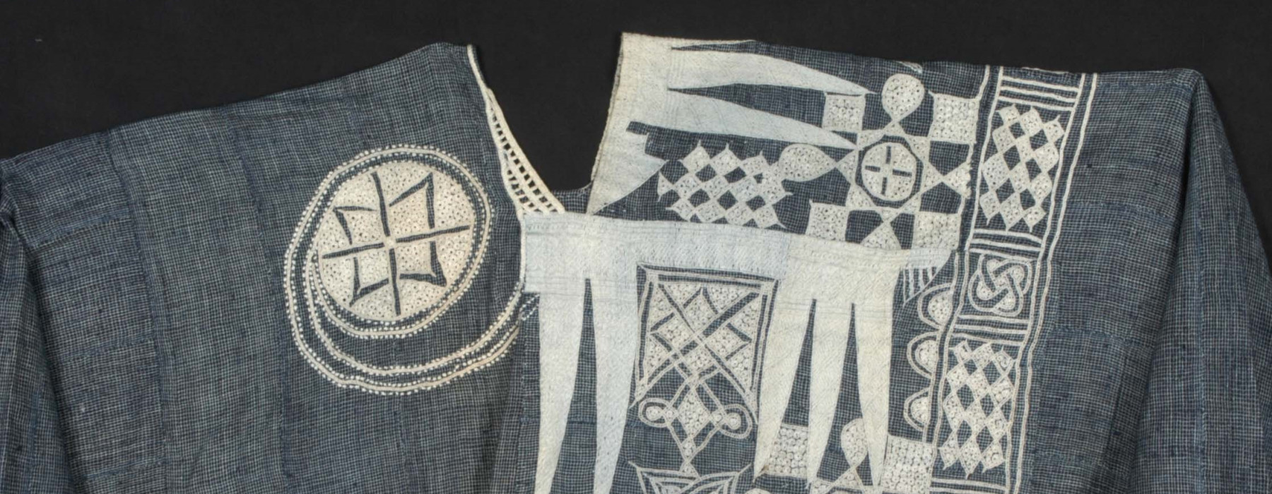 Blauwe katoenen boubou uit het begin van de 20e eeuw, Nigeria. De halslijn en de voorzak zijn versierd met een gedetailleerd wit borduursel met abstracte motieven. (TM-2770-1)