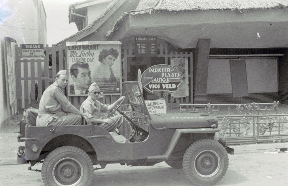 Militairen in een jeep voor een bioscoop met een affiche voor de film 'Mr. Lucky' uit 1943 met Cary Grant en Laraine Day, Batavia (nu Jakarta), Java, mei 1947. (TM-10029130) © Erven C.J. Taillie