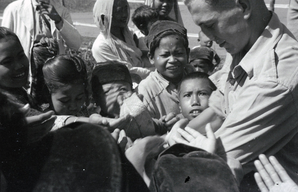 Uitdelende Nederlandse militair omringd door kinderhanden tijdens de feestelijkheden in Cipanas (Java) ter gelegenheid van de geboorte van prinses Marijke (Christina), februari 1947. (TM-10080657) © Erven C.J. Taillie