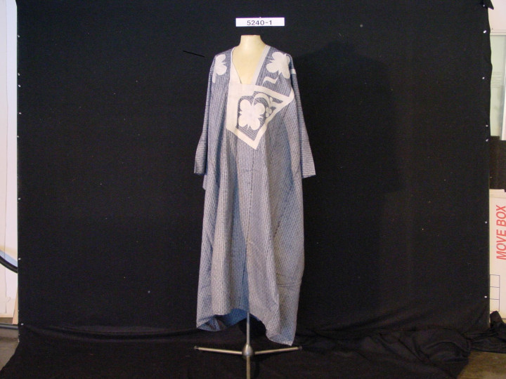 TM-5240-1: Lichtblauwe katoenen boubou uit de 20e eeuw, Mali. De stof is versierd met verticale witte lijnen en op de voorzak zijn witte bloemenborduursels gestikt. (TM-5240-1)