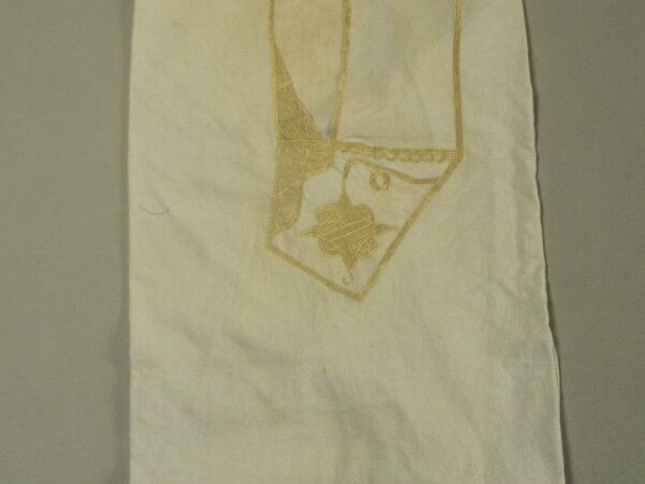 Witte boubou uit de jaren 1980, Mali. De voorzak is versierd met gouden borduursels die de vorm van de zak accentueren, met een bloemachtige vorm in het midden. (WM-67765)